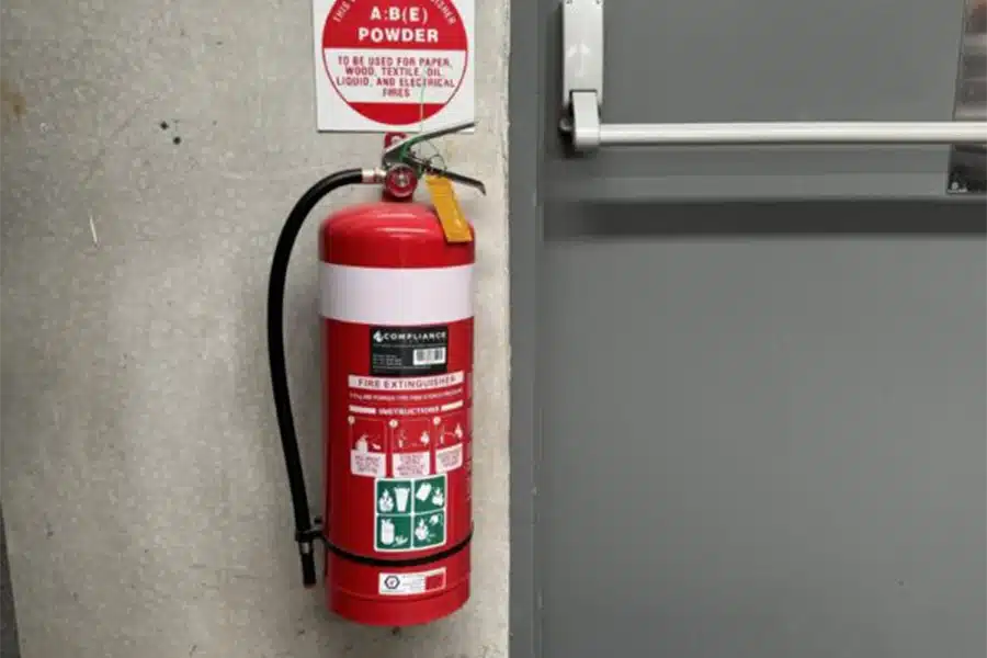 Red ABE powder fire extinguisher mounted next to an emergency exit door