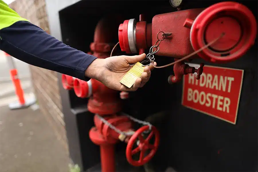 Technician inspecting a red fire hydrant booster with a yellow maintenance tag